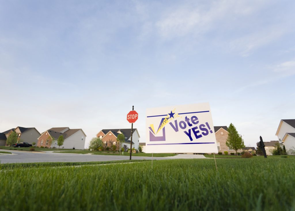 Image of a lawn sign in a neighborhood reading Vote Yes